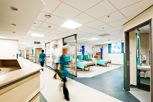medical staff walk past hospital beds in open hallway