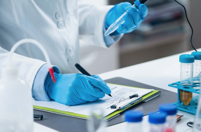 gloved technician records sample assay information on clipboard