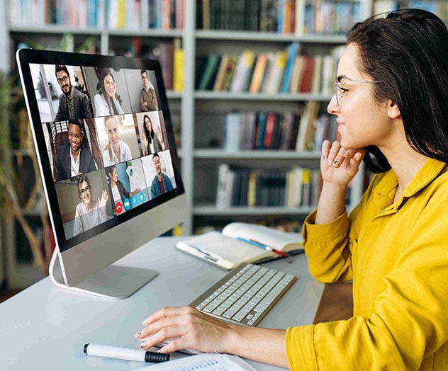 professional seated at desk with open notebook looks at computer showing nine colleagues